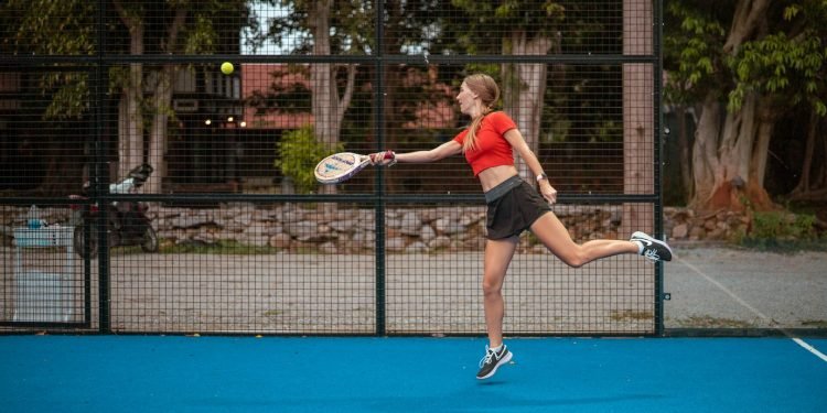 woman in red tank top and black shorts holding tennis racket